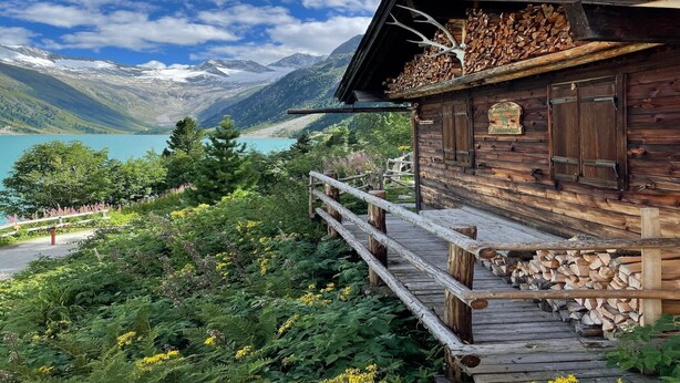 Una cabaña de madera con un porche de madera, rodeada de exuberante vegetación y un paisaje montañoso.