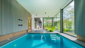Une piscine intérieure moderne avec des parois en verre transparent, une lumière naturelle abondante et une vue sur l’extérieur.