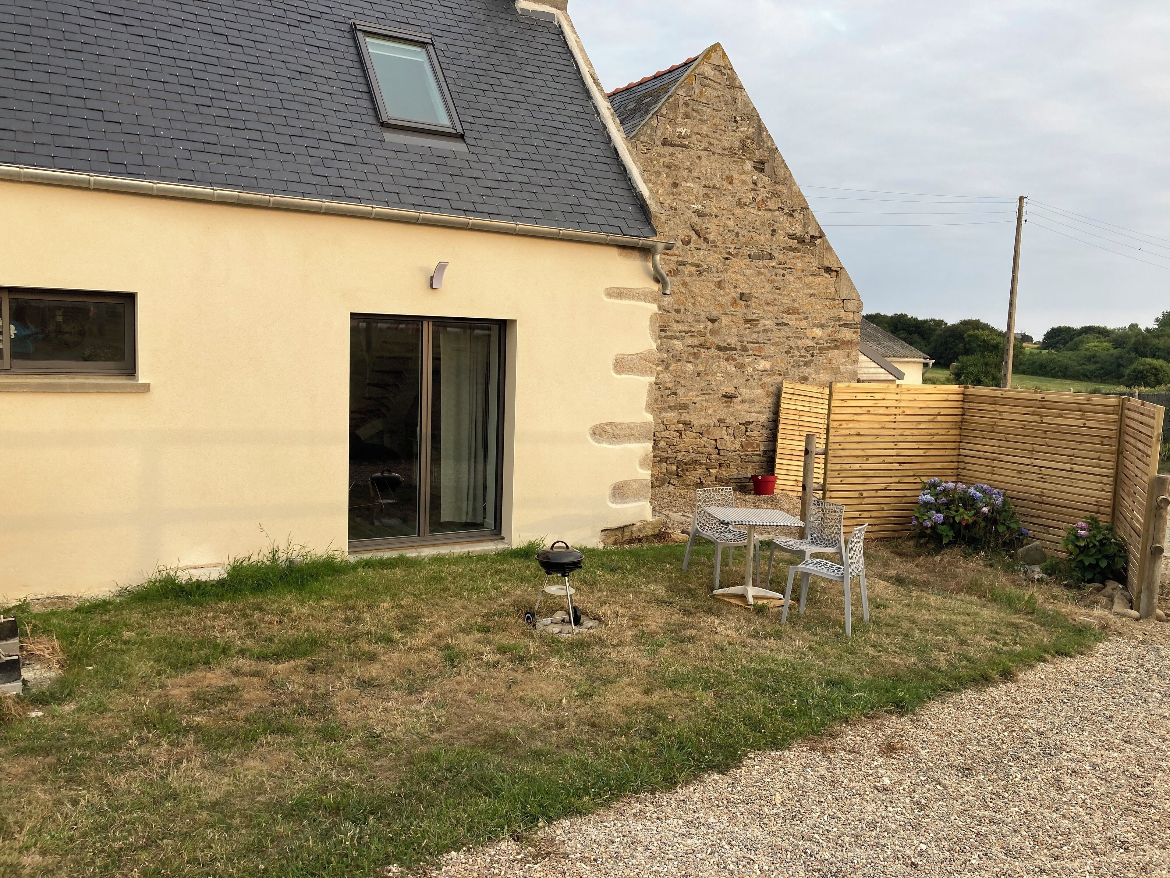 A house with a stone exterior, a large sliding glass door, and a small patio with a barbecue grill and chairs.