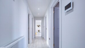 A hallway with white walls, a radiator, and a door with a small window. - Hybrid Resi - Uxbridge | 3 Bed Apartment (Uxbridge)