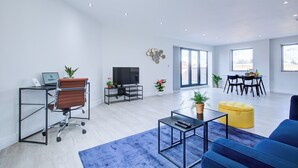 A modern living room with a sofa, coffee table, TV, and a dining area with a table and chairs. - Hybrid Resi - Uxbridge | 3 Bed Apartment (Uxbridge)