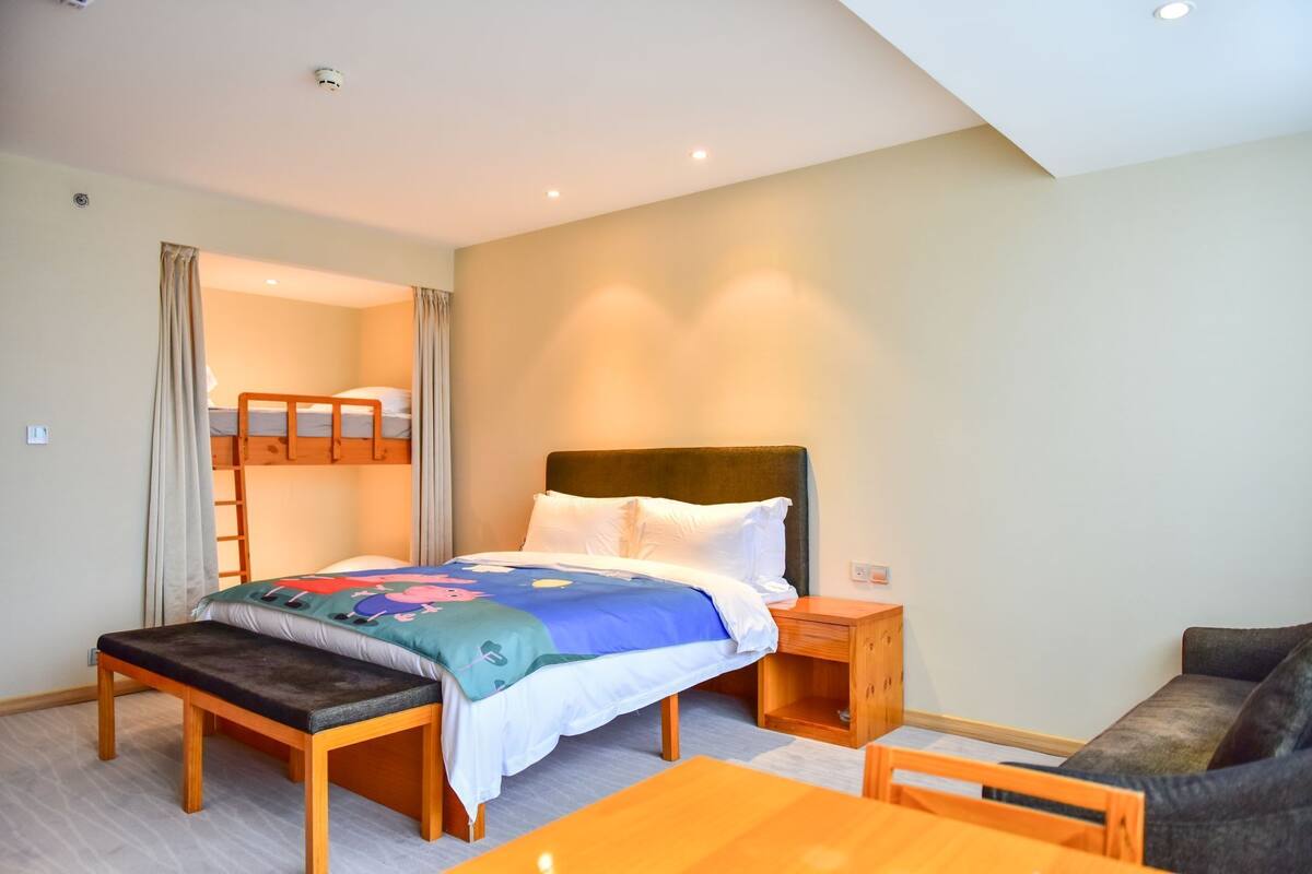 Una habitación con literas, una cama individual, una mesa de madera y un sofá.