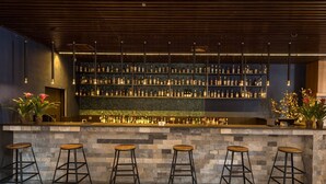 A bar area with a stone counter, multiple shelves of liquor bottles, and four wooden stools. - YunDing Grand Hotel (Zhangjiakou)