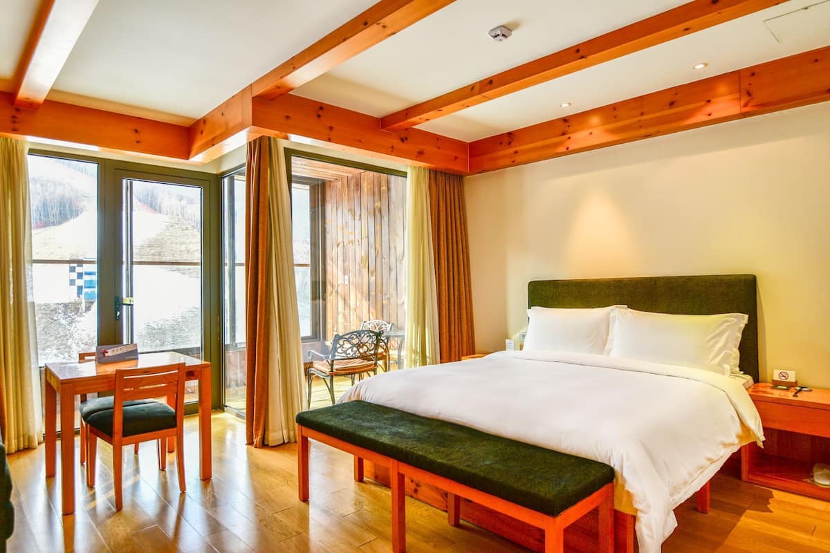 Habitación de hotel con cama, un banco, una mesa con sillas y vistas al exterior.