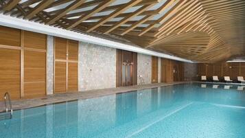 Una piscina interior con paneles de madera, paredes de piedra y suelo de baldosas.