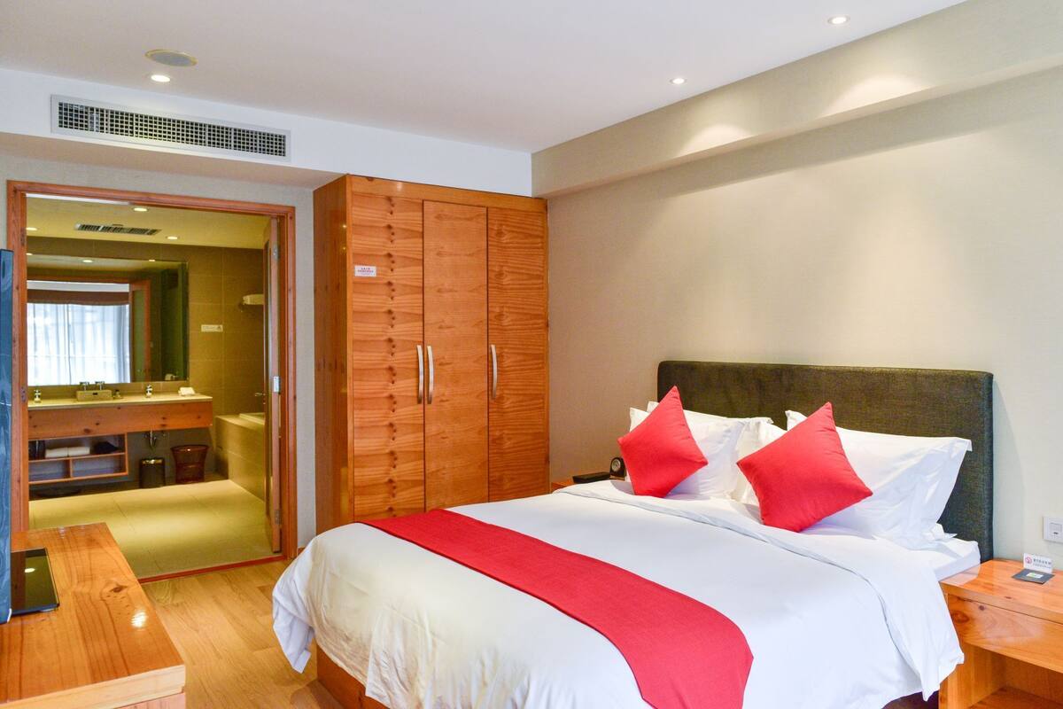 Una habitación de hotel con cama, armario de madera, baño con espejo y mesita de noche.