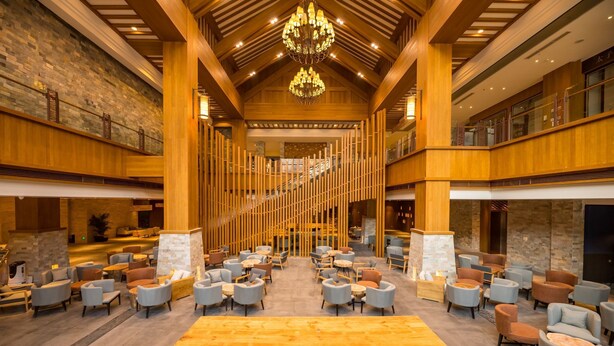 A spacious lobby with a large wooden table and multiple seating areas, featuring a modern chandelier and wooden columns. - YunDing Grand Hotel (Zhangjiakou)