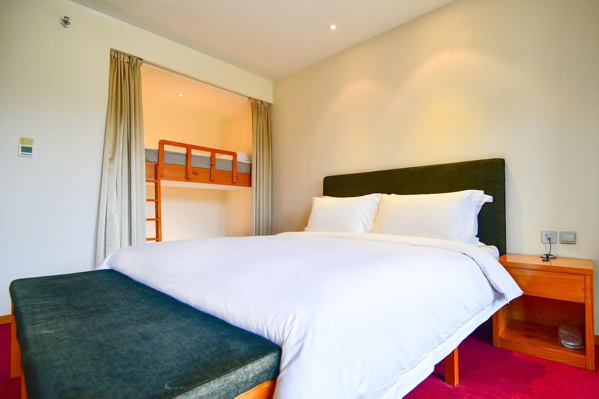 Una habitación de hotel con una cama litera, una cama individual, una mesita de noche y un buró.