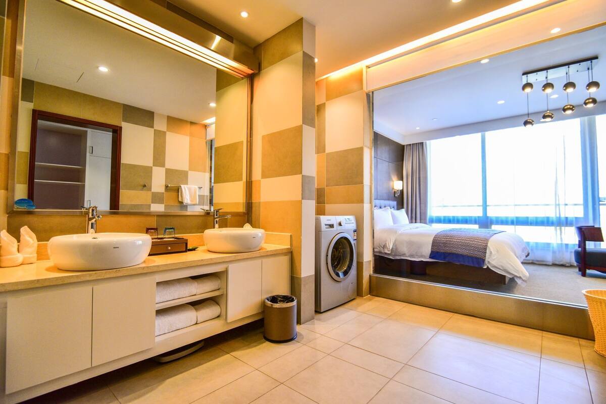 Un baño de hotel moderno con un espejo grande, dos lavabos, una lavadora y un ventanal con vistas.