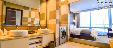 A modern hotel bathroom with a large mirror, two sinks, a washing machine, and a large window with a view.