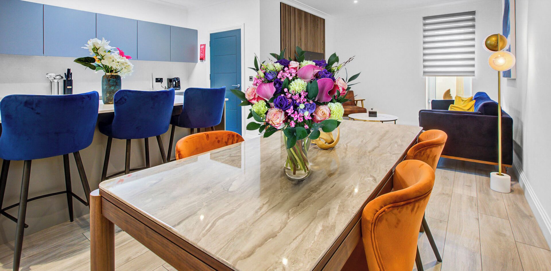 Ein moderner Essbereich mit einem Marmortisch, blauen und orangen Stühlen und einer floralen Tischdekoration.