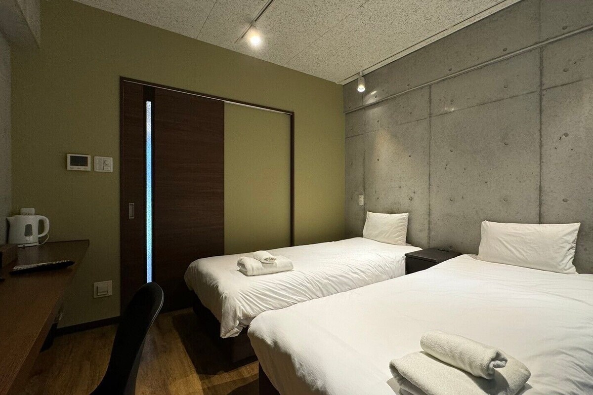 A hotel room with two beds, a desk with a coffee maker, and a wardrobe.
