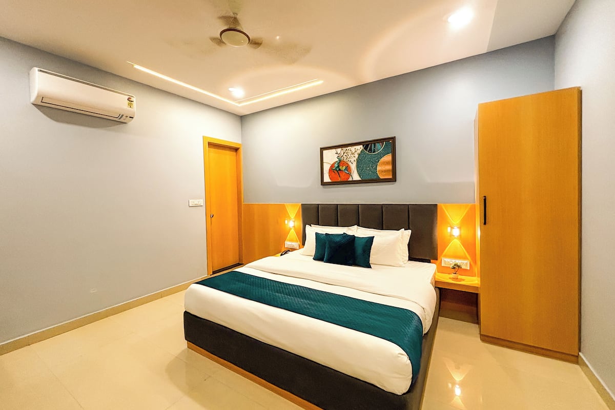 A modern hotel room with a large bed, a ceiling fan, an air conditioning unit, and a painting on the wall.
