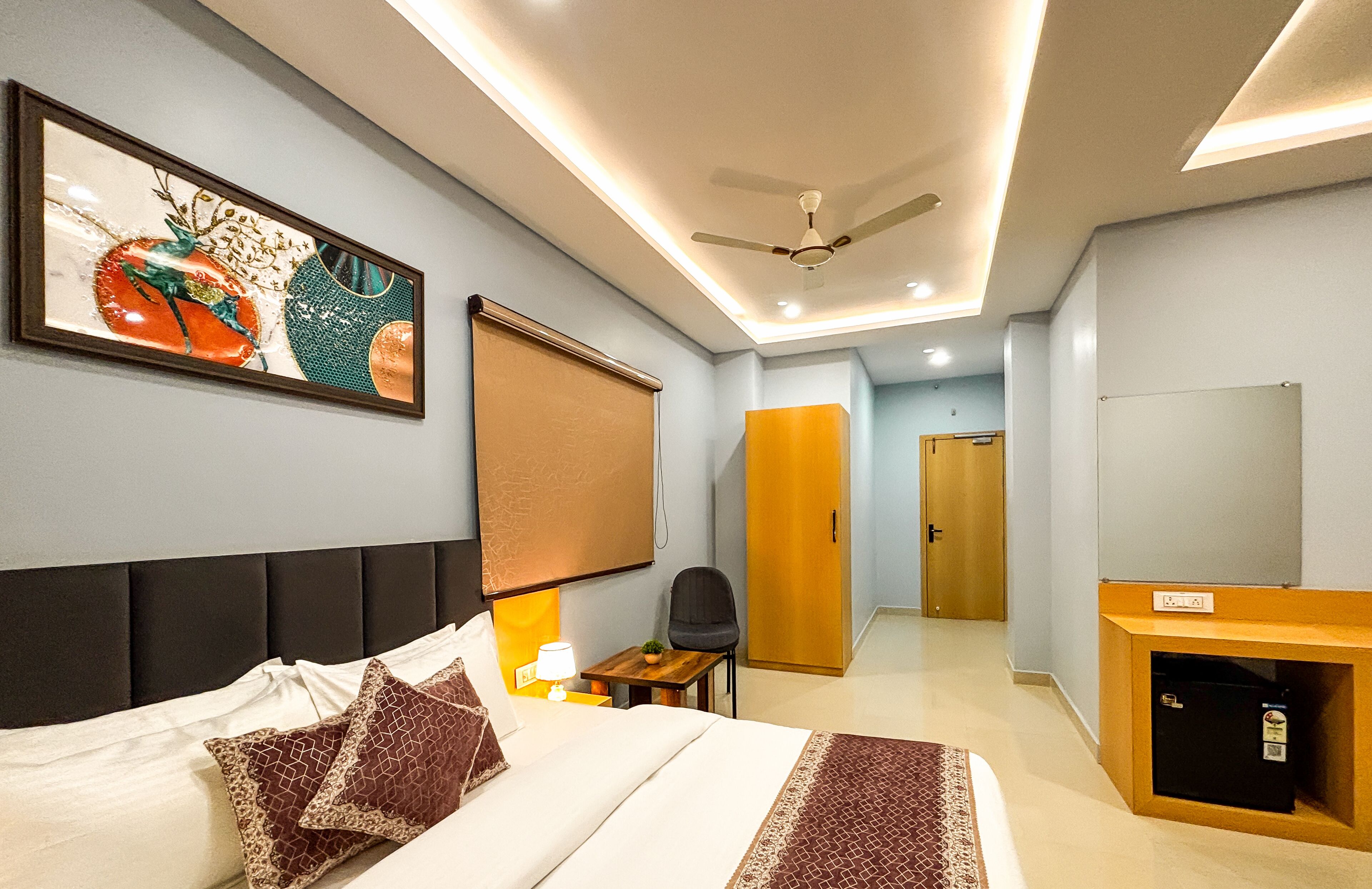 Ein Hotelzimmer mit Bett, Schreibtisch, Stuhl, Kleiderschrank und Deckenventilator.