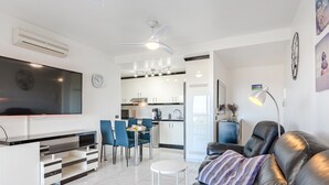 Un salon moderne avec un canapé en cuir noir, un téléviseur à écran plat et un coin repas doté de chaises bleues.