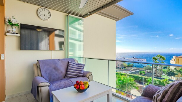 Un balcon avec un canapé, une table avec des fruits, une horloge et un téléviseur.