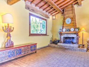 Un interno rustico con un camino, una panca decorata con motivi floreali e una finestra che si affaccia su alberi.