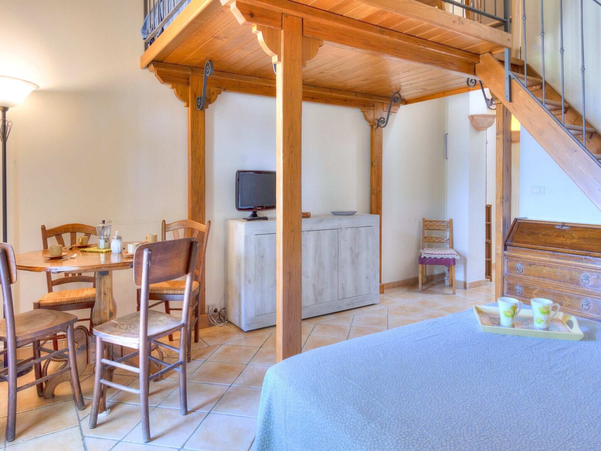 Une pièce chaleureuse avec une table à manger en bois, des chaises, un téléviseur et un lit recouvert d’une couverture bleue.