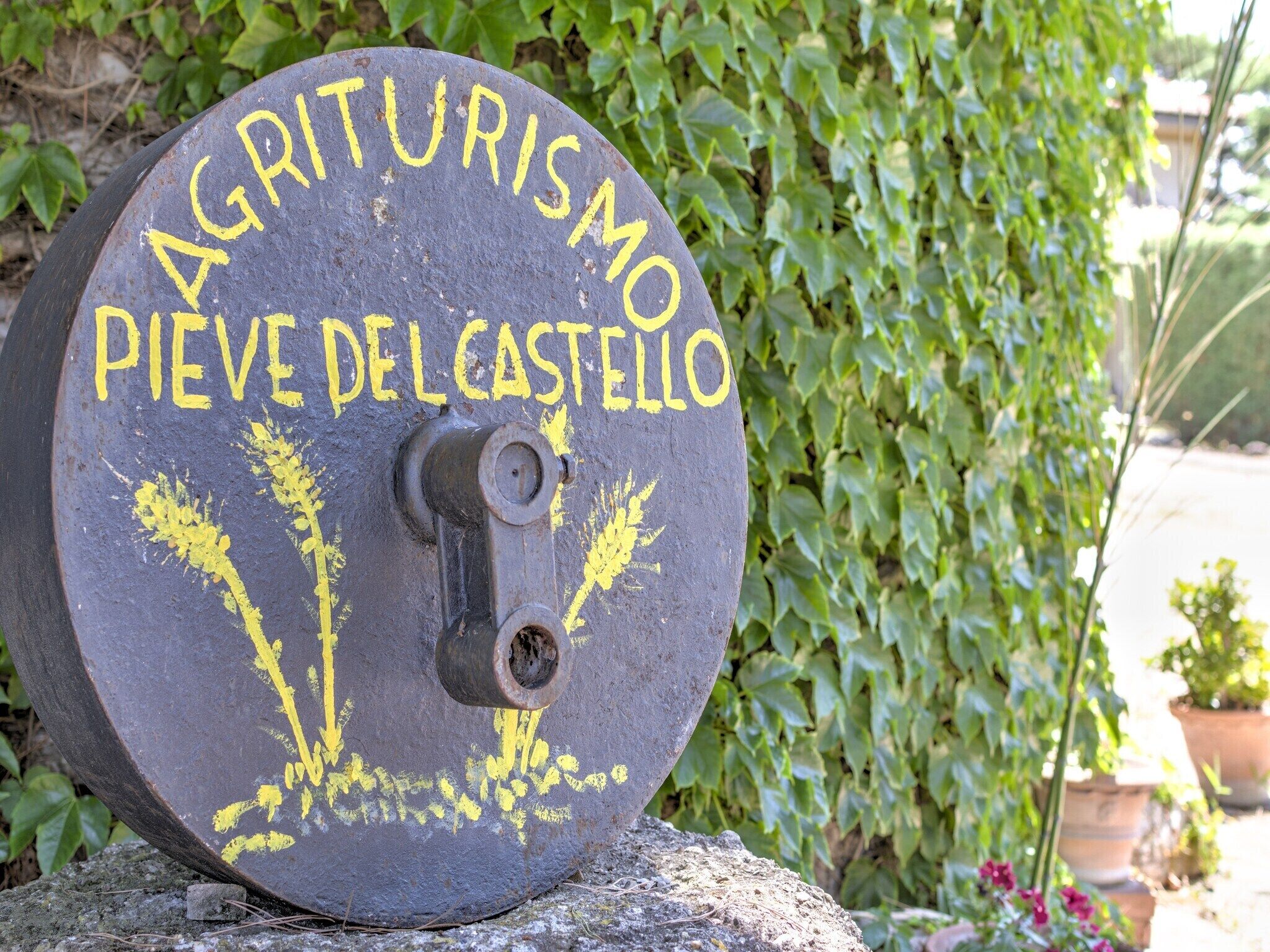 A circular stone with 'AGRITURISMO PIEVE DEL CASTELLO' painted in yellow.