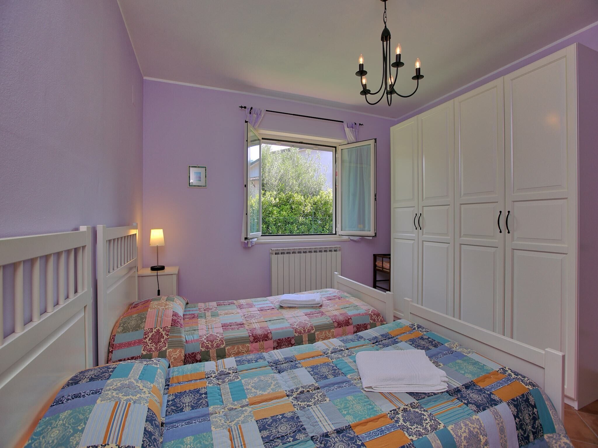 Een slaapkamer met twee bedden, een raam, een radiator en witte kasten.