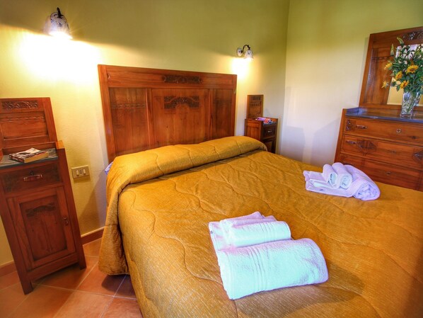A neatly made bed with a wooden headboard, a wooden dresser with a mirror, and a nightstand with a lamp. - Farmhouse in Tuscany near Bibbiano Castle (Montalcino)