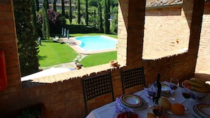 A terrace with a table set for dining, overlooking a swimming pool and lush garden. - Farmhouse in Tuscany near Bibbiano Castle (Montalcino)