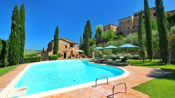 A swimming pool with a brick deck, surrounded by greenery and tall cypress trees. - Farmhouse in Tuscany near Bibbiano Castle (Montalcino)