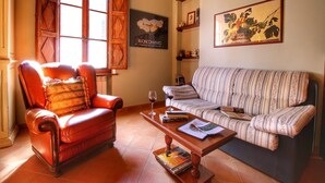 A living room with a leather armchair, a striped sofa, a wooden coffee table, and a window with wooden shutters. - Farmhouse in Tuscany near Bibbiano Castle (Montalcino)