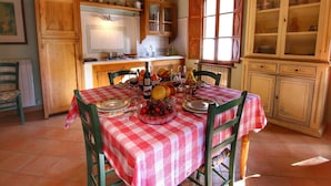 A dining area with a red and white checkered tablecloth, wooden chairs, and a variety of fruits and bottles on the table. - Farmhouse in Tuscany near Bibbiano Castle (Montalcino)