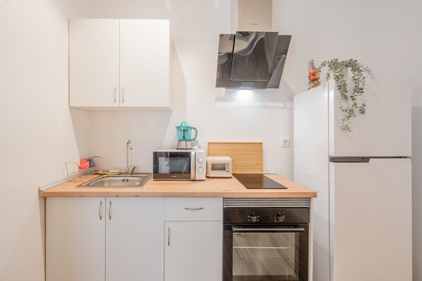 A compact kitchen with white cabinets, a microwave, toaster, kettle, and a dishwasher.