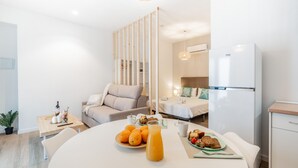 Una habitación moderna y bien iluminada, con una mesa lista para el desayuno, una cama con cabecera de madera y un refrigerador blanco.