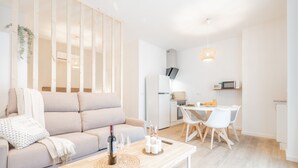 Una sala de estar moderna con un sofá, una mesa de centro con una botella y vasos, y un comedor con sillas y una mesa.