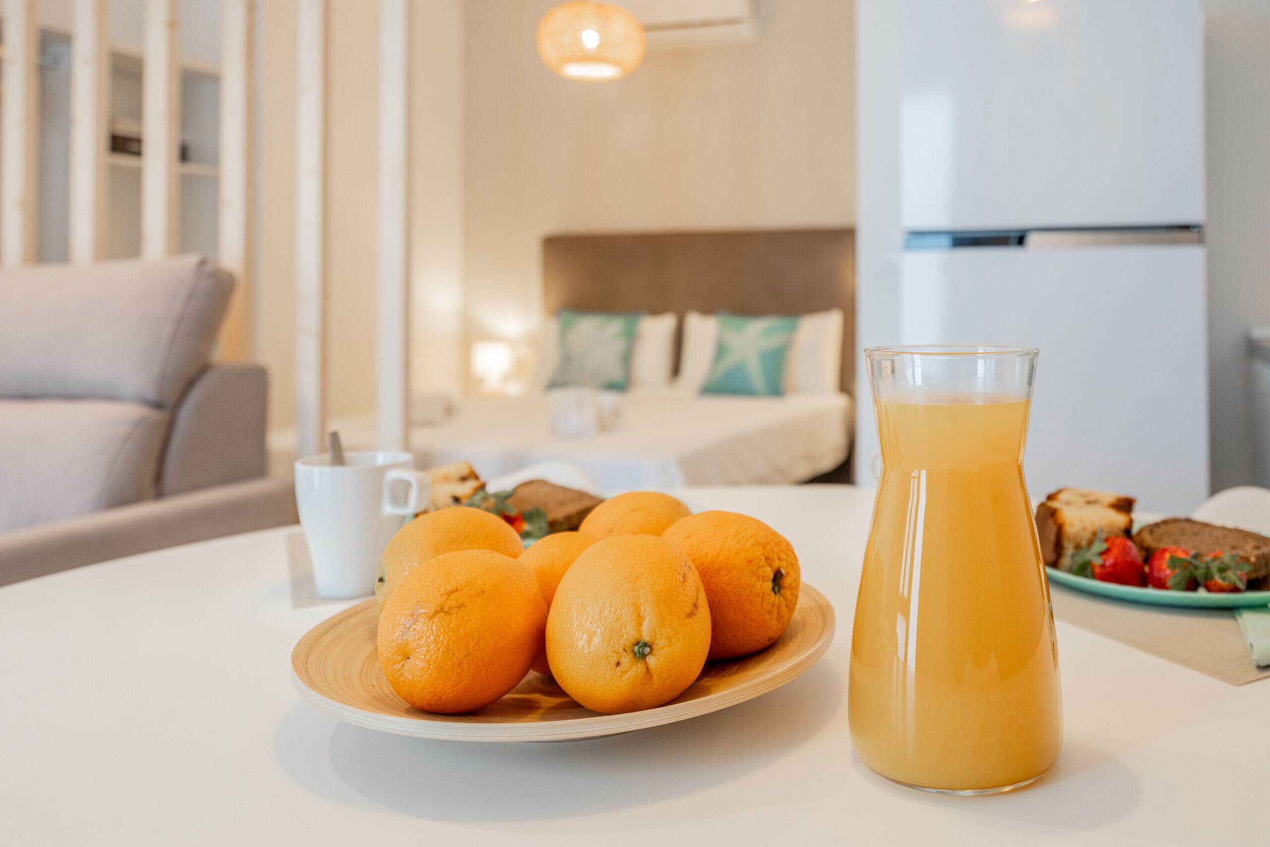 A breakfast setting with oranges on a plate, a glass of orange juice, and a plate of toast and strawberries on a table.