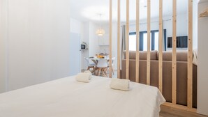 Una habitación de hotel moderna con una cama grande, un separador de madera, un rincón de comedor y vistas a la ciudad.