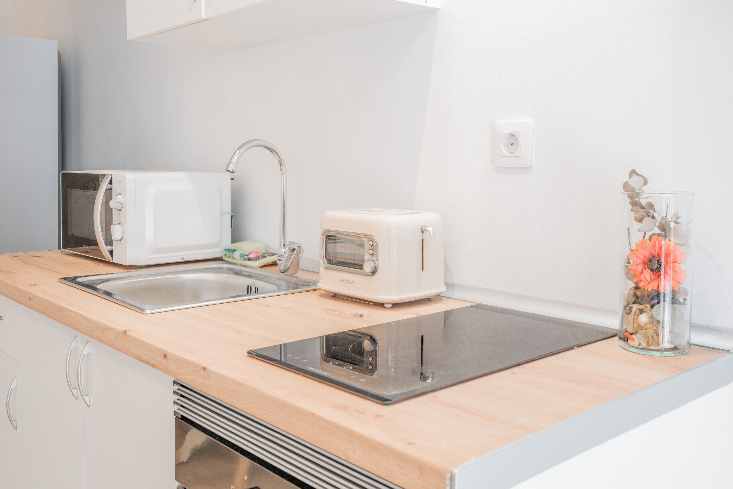 A kitchen with a microwave, toaster, sink, and a decorative glass vase with flowers.