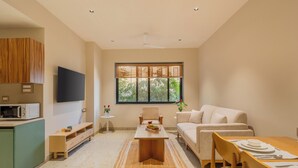 A modern living room with a sofa, a dining table set, a coffee table, and a TV mounted on the wall. - ELIVAAS Kamerios Verano 1 BHK with Pool (Marra)