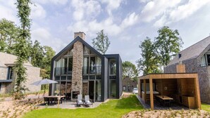 Ein modernes Haus mit einer Stein-Fassade, großen Fenstern und einer Terrassenanlage mit Gartenmöbeln.