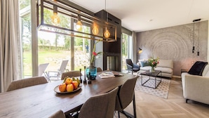 Ein modernes Wohnzimmer mit Essbereich, großen Fenstern und einem Kamin.