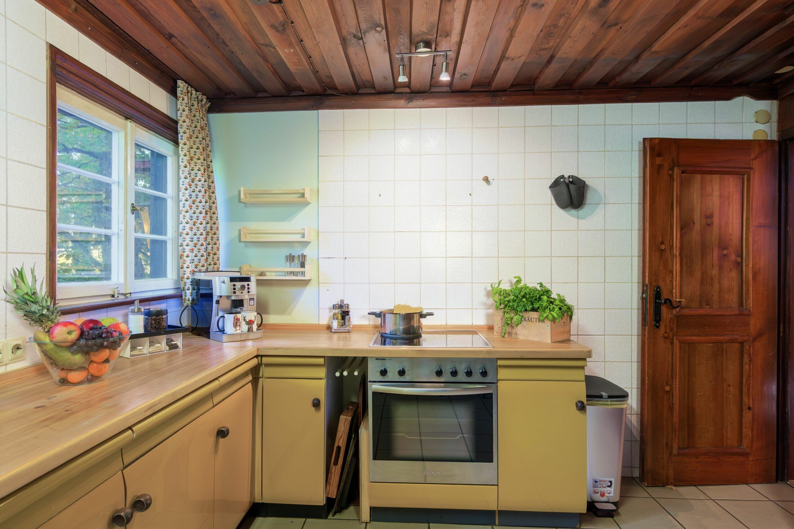 Una cocina con gabinetes de madera, una estufa, un fregadero y una ventana con cortina.