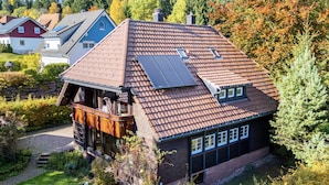 Et hus med skråt tag, solpaneler og en balkon med udendørs møbler.