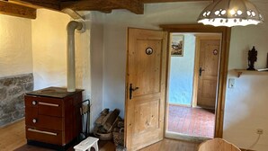 Una habitación rústica con paredes y techo de madera, una estufa, un pequeño banco de madera y una puerta que da a otra habitación.
