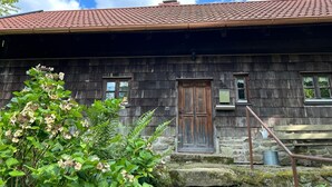 Un edificio rústico de madera con tejado de tejas rojas, una puerta de madera y una pequeña ventana.