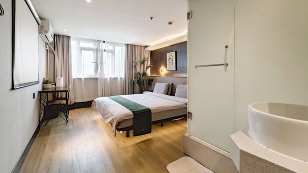 A modern hotel room with a large bed, a desk, a chair, a vanity with a bathtub, and a window with curtains. - Iforest Hongkou Football Stadium (Shanghai)