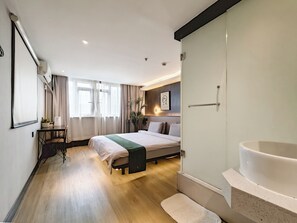 A modern hotel room with a large bed, a desk, a chair, a vanity with a bathtub, and a window with curtains. - Iforest Hongkou Football Stadium (Shanghai)