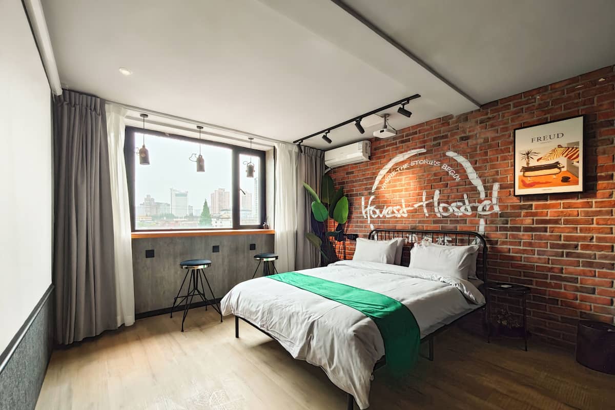 A modern bedroom with a brick wall, a large bed, a city view, and a ceiling-mounted projector.