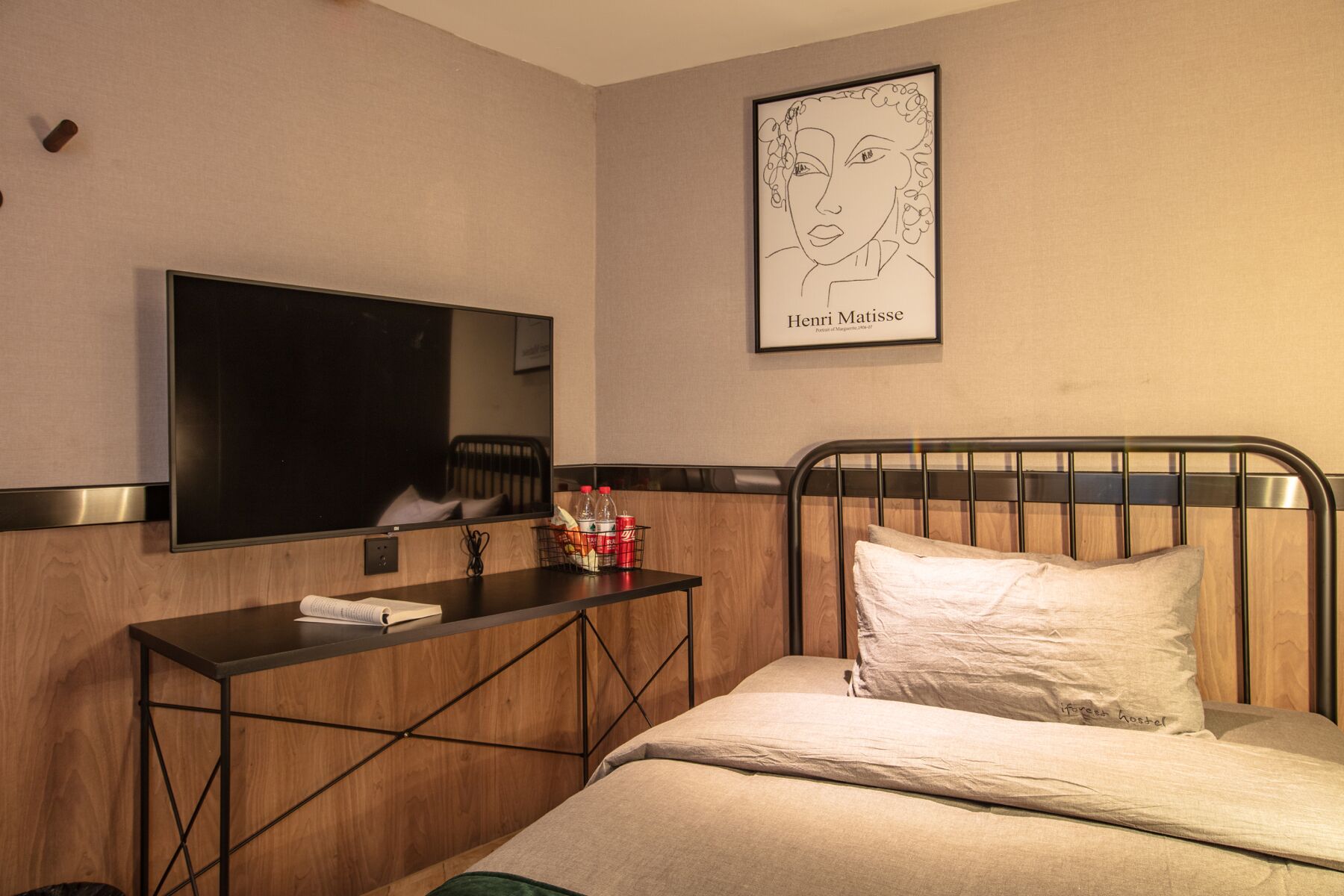 A hotel room with a bed, a bedside table with a TV, a framed artwork of Henri Matisse, and a wooden headboard.