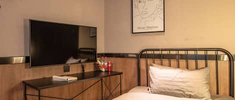 A hotel room with a bed, a bedside table with a TV, a framed artwork of Henri Matisse, and a wooden headboard.