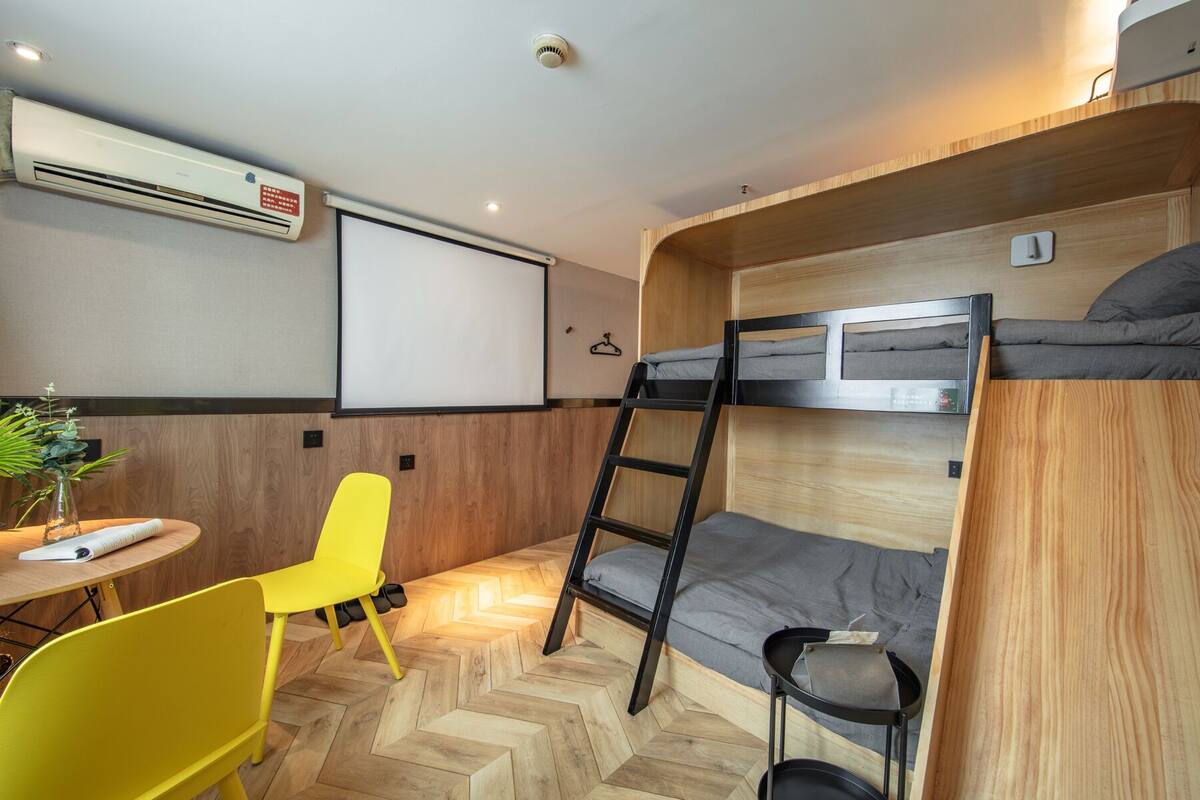 A compact room with bunk beds, a desk, a chair, and an air conditioning unit.