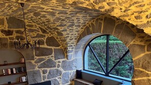 Un interior acogedor con pared de piedra, un ventanal grande, sofá empotrado y estantería.