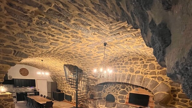 Un interior con techo y chimenea de piedra, un sofá y un comedor con sillas y una mesa.